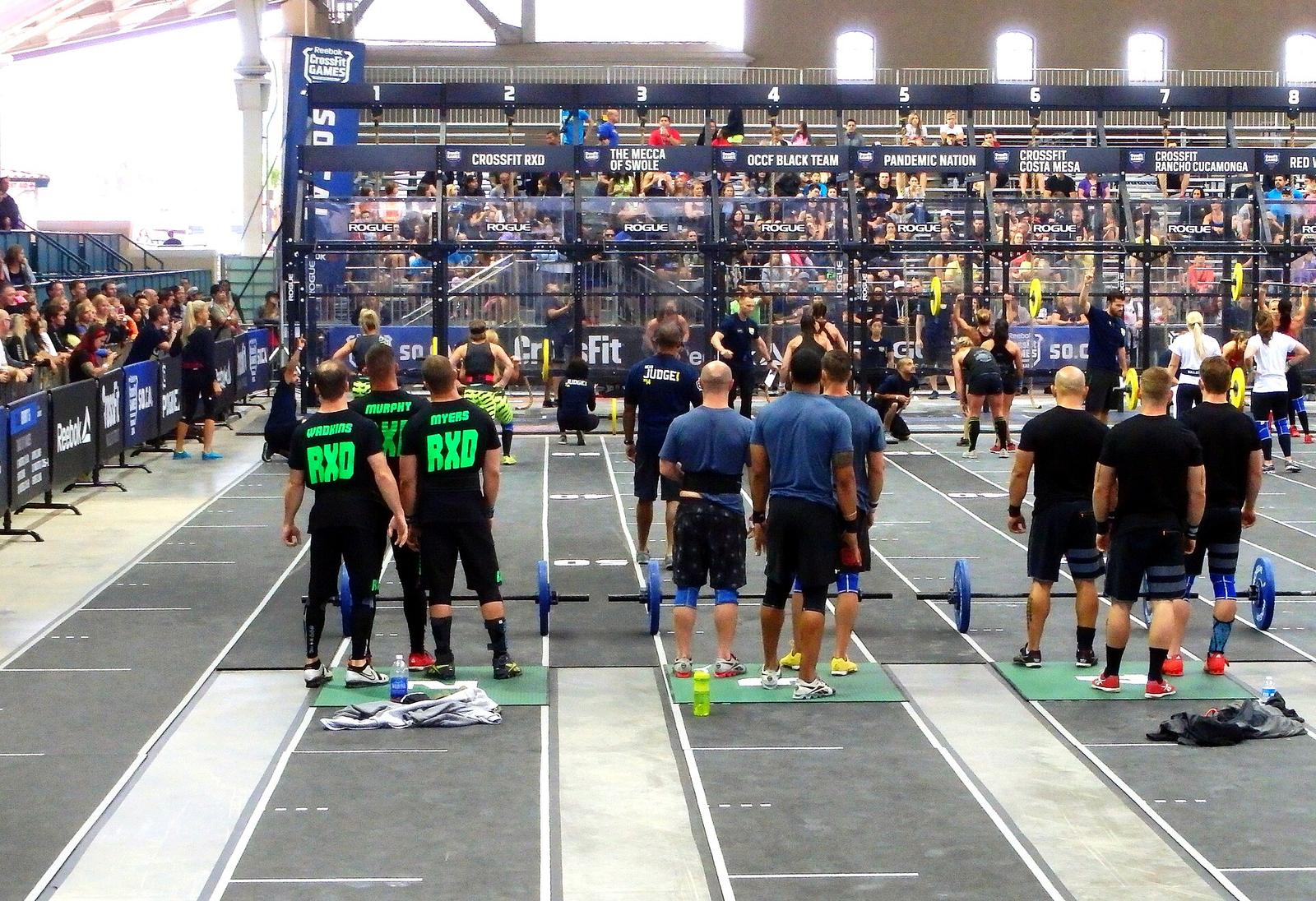 Teams lined up at barbell stations in an arena at a CrossFit regional